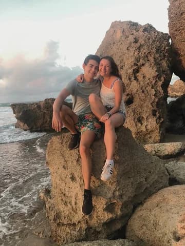 Allie and Alex sitting close together on a large pale boulder at the water's edge at sunset.