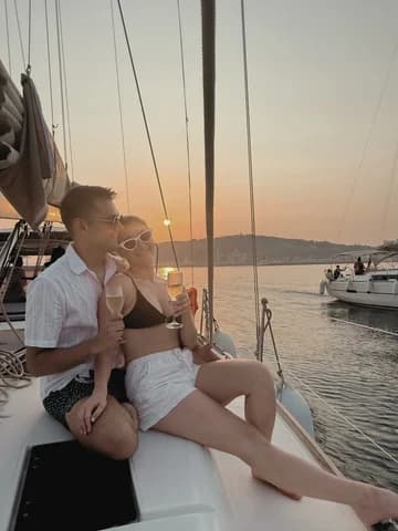 Allie and Alex sitting on the foredeck of a sailboat at sunset, holding champagne glasses.