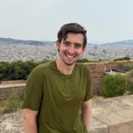 Groomsman: a man in an olive-green t-shirt at a stone parapet, a wide city panorama and hills behind him.