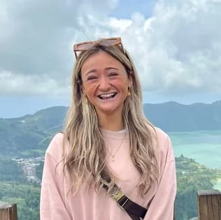 Maid of Honor: a woman with long blonde hair and sunglasses pushed up on her head, laughing, a green crater lake behind her.